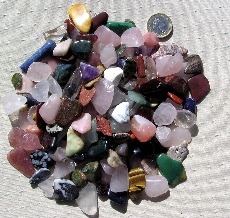 Puede incluir: Una colecci&oacute;n de piedras pulidas de varios colores y formas, incluyendo rosa, verde, marr&oacute;n y azul. Las piedras est&aacute;n dispuestas en una pila sobre un fondo de tela blanca.