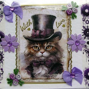 Op de afbeelding: Een rechthoekige wenskaart met een centrale illustratie van een pluizige bruine kat met een donkere hoge hoed en een paarse vlinderdas. De tekst "With Love" is in goud gedrukt. De kaart is versierd met paarse stoffen strikken en papieren bloemen.