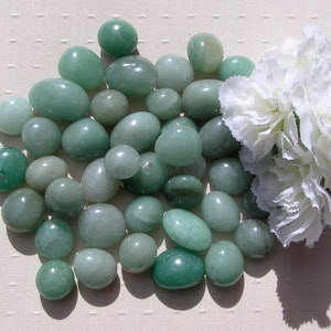 Puede incluir: Una colecci&oacute;n de piedras lisas y verdes, probablemente de aventurina o jade, dispuestas sobre una superficie blanca. Las piedras son de varios tama&ntilde;os y formas, algunas parecen m&aacute;s redondeadas que otras.
