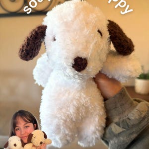 May include: A white plush puppy toy with dark brown ears and a dark brown nose. The text soup belly puppy is written in white above the toy, and the text original creator is written in white below. The toy has a soft, fuzzy texture.