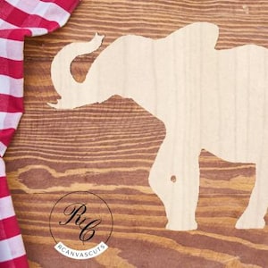 May include: A white wooden elephant silhouette cutout on a brown wood background. The elephant is facing right and has its trunk raised.