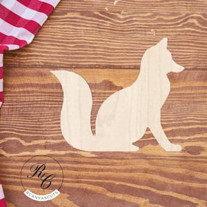 May include: A white wooden cutout of a fox sitting on a brown wooden surface. The fox is facing the right side of the image.