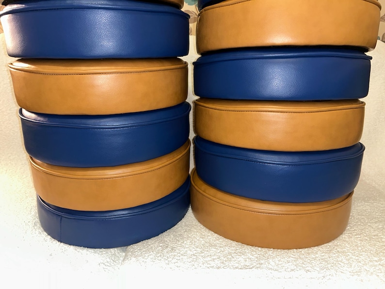 Puede incluir: Una pila de seis cojines redondos, alternando tela azul y marr&oacute;n. Los cojines est&aacute;n apilados en dos columnas.