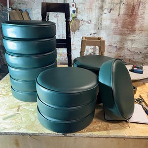 Puede incluir: Una pila de taburetes de bar redondos de color verde oscuro con base de madera. Los taburetes est&aacute;n apilados sobre una superficie de madera.