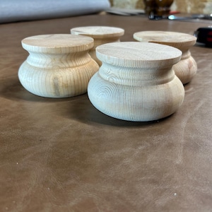 Puede incluir: Cuatro patas de muebles de madera sin terminar, cada una con una parte superior redondeada y una forma bulbosa y torneada. La veta de la madera es visible y las patas están dispuestas sobre una superficie marrón. Son piezas de repuesto.