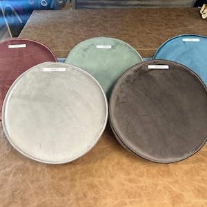May include: Five circular velvet fabric samples in shades of dusty rose, sage green, light grey, dark brown, and teal. Each sample has a white label. The samples are displayed on a brown leather surface.
