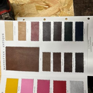 Puede incluir: Una carta de colores de muestras de cuero para tapicer&iacute;a. Las muestras est&aacute;n dispuestas en filas y columnas, con cada muestra etiquetada con un nombre de color. Los colores incluyen crema antigua, cebada, escarlata, burdeos, ciruela, espacio, atl&aacute;ntico, marr&oacute;n, arena, caoba, marr&oacute;n antiguo, cacao, amarillo, rosa beb&eacute;, rosa intenso, rojo, plata y agua.