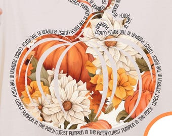 May include: Ivory-colored t-shirt featuring a pumpkin design filled with flowers in shades of orange, yellow, and white. The text "CUTEST PUMPKIN IN THE PATCH" encircles the pumpkin. A round "ivory" label is visible.