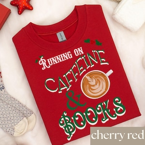 May include: Cherry red sweatshirt with the text "Running on Caffeine & Books" in white and green. A coffee cup graphic is featured in the center. The sweatshirt is a crew neck style.
