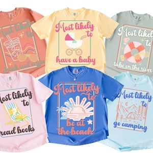 Puede incluir: Seis camisetas de colores brillantes, cada una con un gráfico diferente y la frase "Most likely to" seguida de una actividad. Los diseños incluyen "leer libros", "estar en la playa" y "acampar".