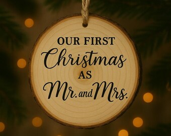 May include: A round wooden Christmas ornament with the text "OUR FIRST Christmas as Mr. and Mrs." in black script. The ornament is suspended by a natural twine string against a blurred background of Christmas tree branches and bokeh lights.