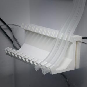 May include: White plastic pipe holder with multiple slots for organizing pipes. The holder is mounted to a wall and has a curved design.