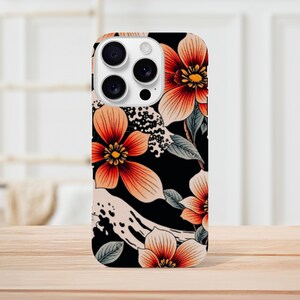 Peut inclure: Une coque de téléphone noire avec un motif floral. Les fleurs sont orange, rose et blanche avec des contours noirs. La coque de téléphone a un renflement de caméra blanc avec trois objectifs noirs.