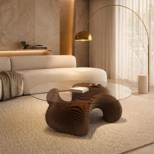 May include: A coffee table featuring a circular glass top resting on a dark brown, sculptural wooden base with layered, wave-like horizontal slats. The base has a fluid, organic shape that supports the transparent surface from below.