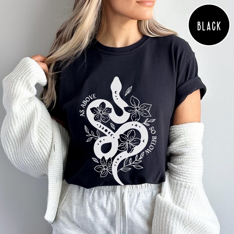 Pu&ograve; includere: T-shirt nero con grafica bianca di un serpente intrecciato con fiori e la scritta "AS ABOVE SO BELOW". La maglietta &egrave; a girocollo.