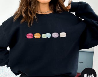 May include: Black sweatshirt with a row of colorful macarons printed on the front. The macarons are pink, orange, green, blue, and purple.
