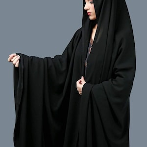 Puede incluir: Una abaya negra con un diseño largo y fluido. La abaya tiene una capucha y está hecha de una tela suave y ligera.