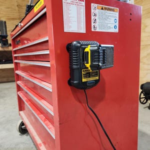 May include: A red rolling tool chest with multiple drawers and a black and yellow DeWalt battery charger attached. The chest has silver trim and is on wheels. A warning label and a list are affixed to the side.