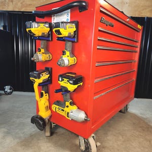 May include: A red rolling tool chest with multiple drawers and a black handle. Several yellow and black power tools are mounted on the side. The tools include drills and impact wrenches, with black and blue mounting brackets.
