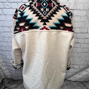 May include: A cream-colored fleece jacket with a geometric pattern on the back and cuffs. The pattern is in shades of black, brown, blue, and red.