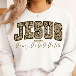 May include: White sweatshirt featuring the word "JESUS" in large leopard print lettering. The text "JOHN 14:6" and the phrase "the way, the truth, the life" are below the word "JESUS" in a gold script font.