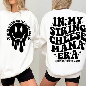 Könnte beinhalten: Weißes Sweatshirt mit schwarzer Grafik auf Vorder- und Rückseite. Die Vorderseite zeigt einen schmelzenden Smiley mit dem Text "IN MY STRING CHEESE MAMA ERA". Die Rückseite hat denselben Text in größerer Schrift mit dem Hashtag #STRINGCHEESEMAMA.