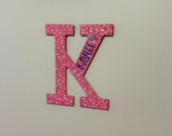 Può includere: Lettera K di glitter rosa con il nome "Kailee" scritto in glitter argento.
