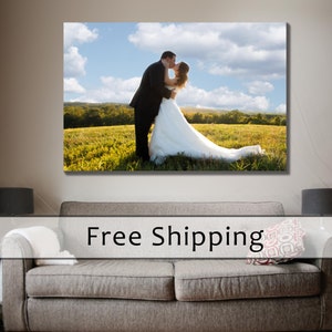 May include: A large canvas print of a couple kissing in a field of green grass under a blue sky with white clouds. The man wears a black suit, and the woman wears a white wedding dress.