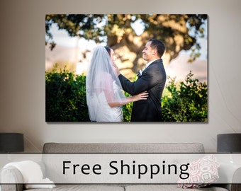 May include: A framed photograph of a couple on their wedding day, displayed above a gray sofa. The couple is embracing outdoors, with the bride in a white dress and veil, and the groom in a black suit. The background features greenery.