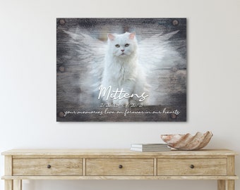 May include: A white cat with angel wings on a wooden background. The cat's name is Mittens and the dates 2/20/08-7/20/21 are written below the cat. The text "your memories live on forever in our hearts" is written below the dates.