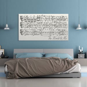 May include: A bedroom with a light blue wall and a bed with a brown comforter and blue pillows. A framed piece of sheet music with the words "The World to Me" hangs above the bed.