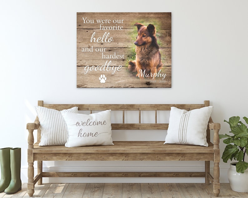 Op de afbeelding: Een houten bord met een foto van een hond en de tekst: "Je was onze favoriete hallo en ons moeilijkste afscheid", met de naam van de hond "Murphy". Het bord staat boven een houten bank met kussens.