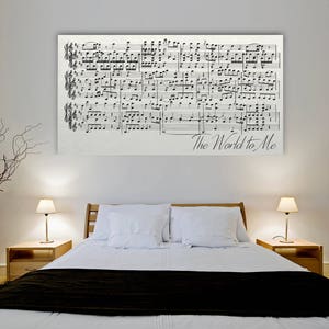 May include: A white bed with a black and white sheet and a black throw blanket. There are two lamps on nightstands on either side of the bed. A framed print of sheet music with the words "The World to Me" is hanging on the wall above the bed.