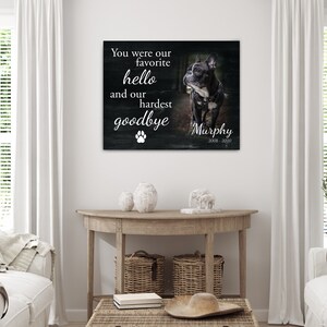 Op de afbeelding: Een ingelijste canvas print met een zwart-wit foto van een hond genaamd Murphy. De tekst luidt: "Je was onze favoriete hallo en ons moeilijkste afscheid" met een pootafdruk en de jaren 2008-2020.