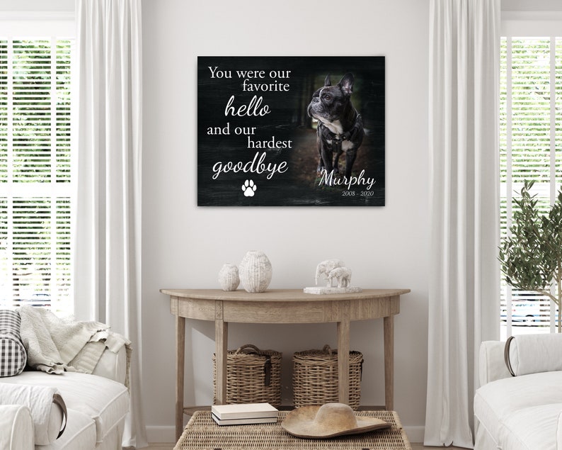 Op de afbeelding: Een ingelijste canvas print met een zwart-wit foto van een hond genaamd Murphy. De tekst luidt: "Je was onze favoriete hallo en ons moeilijkste afscheid" met een pootafdruk en de jaren 2008-2020.