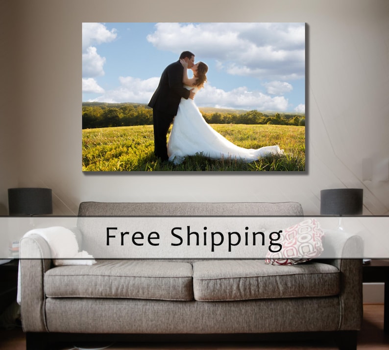 May include: A large canvas print of a couple kissing in a field of green grass under a blue sky with white clouds. The man wears a black suit, and the woman wears a white wedding dress.