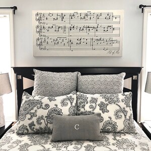 May include: A black bed frame with a white and gray patterned duvet and pillows. The headboard has a decorative molding. A framed print of sheet music with the words "All of Me" is hanging above the bed.