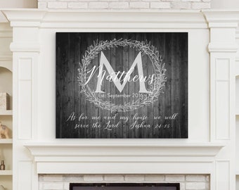 May include: A black and white canvas print with a rustic wood background. The print features a white wreath with the letter "M" and the name "Matthews" inside. The text "Est: September 2016" is below the wreath. The quote "As for me and my house we will serve the Lord - Joshua 24:15" is below the name.