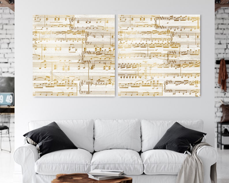 May include: Two white canvas prints with gold musical notes printed on them. The prints are hanging on a white wall above a white couch.