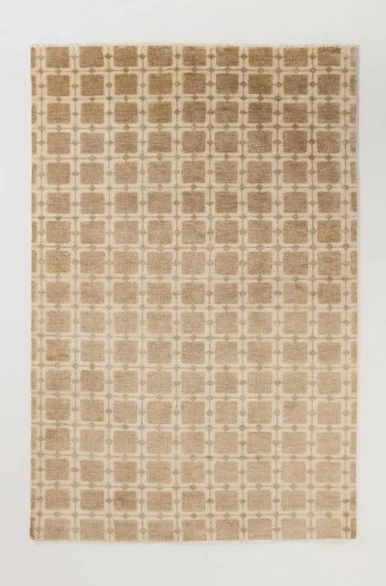 May include: A rectangular rug with a repeating pattern of squares and small connecting dots. The rug has a neutral color palette of beige and light brown, creating a subtle, textured design. The rug is suitable for a living room or bedroom.