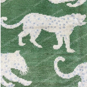 May include: Green rug with a repeating pattern of white cheetahs with blue spots. The rug has a textured appearance, with the cheetahs in various poses. The background is a solid, deep green color.