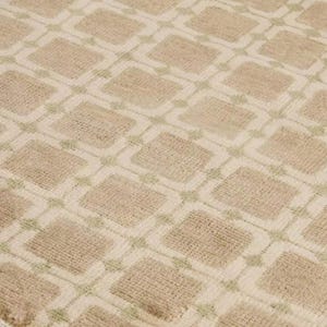 May include: Close-up of a beige rug with a repeating geometric pattern. The design features squares within squares, outlined in a lighter beige and pale green. The rug has a textured, woven appearance.