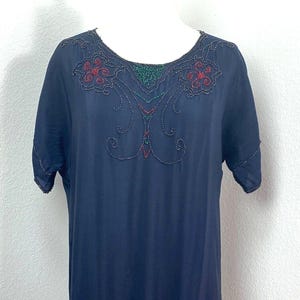 May include: A navy blue dress with short sleeves and a round neckline. The dress is adorned with intricate beaded floral patterns in red, green, and blue. The embellishments are concentrated around the neckline and hemline, adding a touch of elegance.