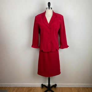 May include: A red suit with a skirt and a blazer. The blazer has a notched collar and four buttons down the front. The skirt is knee-length.