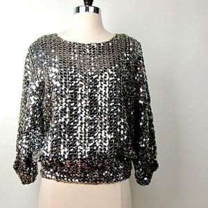 Top pullover vintage anni '80 con paillettes argentate, taglia M, con tre bandiere USA, maniche raglan, vita elasticizzata e canotta nera abbinata, ideale per serate formali, club e vacanze.