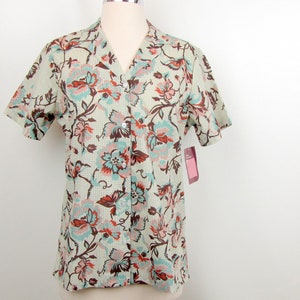 May include: A short-sleeved button-down shirt with a floral print in shades of brown, pink, and blue on a light green background.