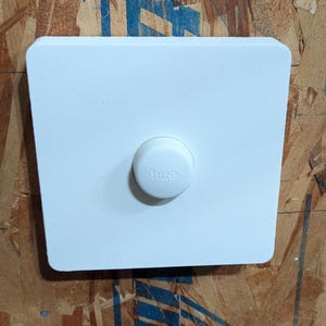 May include: White square wall plate with a round white button that says "hue" on it.