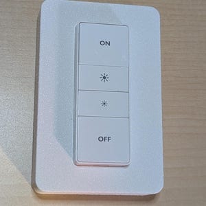 May include: A white smart light switch with four rectangular buttons. The top button reads "ON", followed by two buttons with a lightbulb icon, and the bottom button reads "OFF". The switch is mounted on a white rectangular plate.