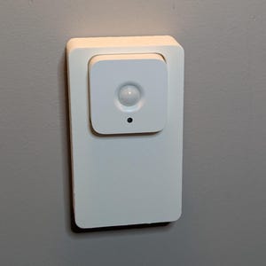 May include: A white motion sensor with a round lens, mounted on a wall.