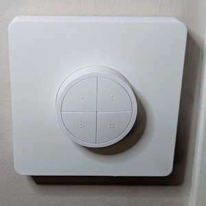 May include: A white, square-shaped light switch with a circular control. The circular control is divided into four sections, each with a series of small dots. The switch is mounted on a wall.